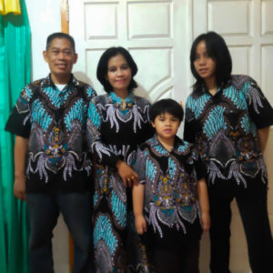 Four people smiling and standing in front of a white door. They are all wearing the same outfit of blue and turquoise patterned shirts.